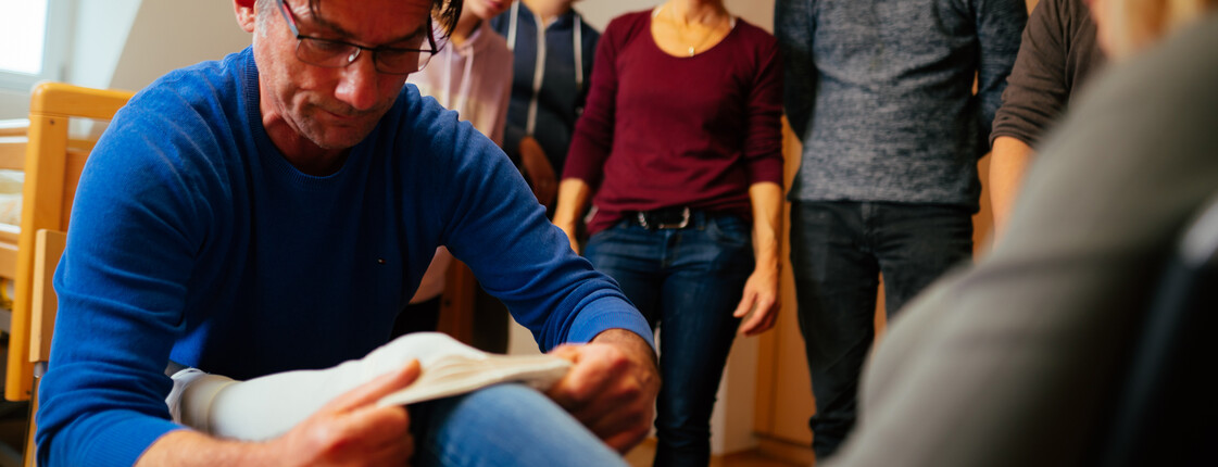 Ein erwachsener Mann zieht einer Mitschülerin einen Kompressionsstrumpf an, die restlichen Mitschüler*innen und die Lehrerin sehen im dabei zu.