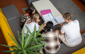 Vier Schüler*innen sitzen auf der Couch im Gemeinschaftsraum und sehen gemeinsam in ihre Schulunterlagen.