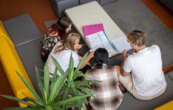 Vier Schüler*innen sitzen auf der Couch im Gemeinschaftsraum und sehen gemeinsam in ihre Schulunterlagen.