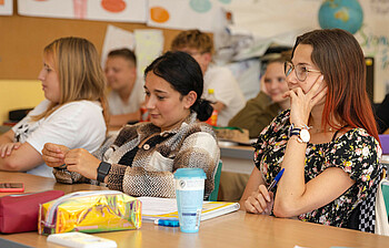 Schülerinnen sitzen interessiert in der Klasse und lauschen der Lehrkraft.