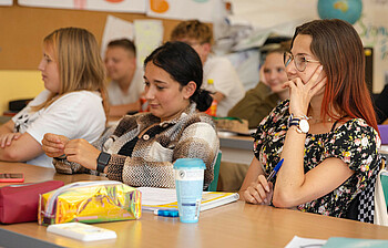 Schülerinnen sitzen interessiert in der Klasse und lauschen der Lehrkraft.